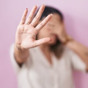 mujer tapándose la cara y con la mano abierta haciendo stop