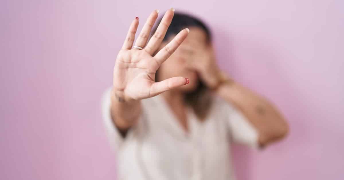 mujer tapándose la cara y con la mano abierta haciendo stop
