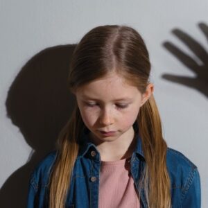 niña mirando al suelo y sombra de una mano a punto de pegarle